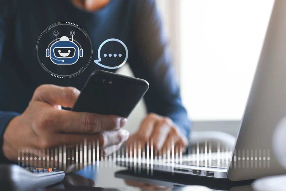 Personne utilisant simultanément smartphone et ordinateur portable dans environnement de travail moderne près d'une fenêtre