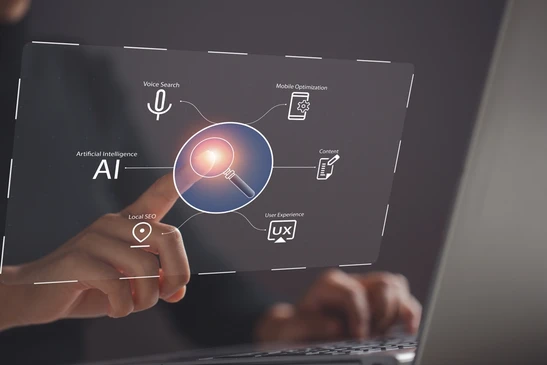 Personne utilisant un ordinateur portable dans un environnement professionnel sombre, pointant vers une interface holographique centrée sur une icône de recherche lumineuse