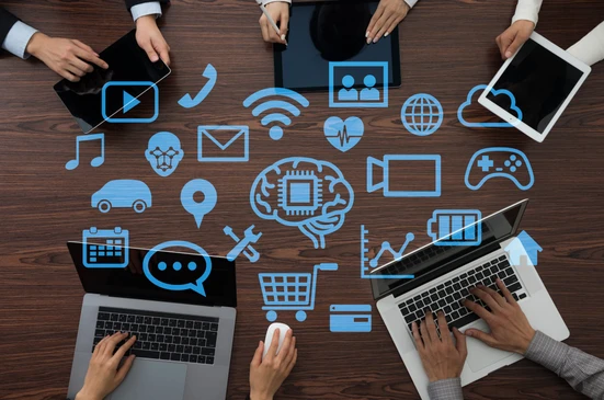 Espace de travail collaboratif avec quatre personnes utilisant ordinateurs portables et tablettes autour d'une table en bois
